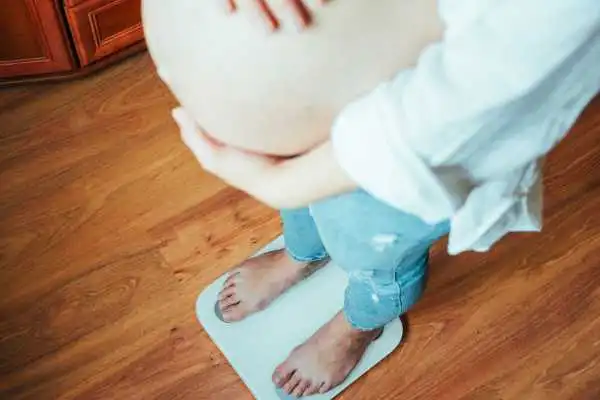 Image of woman weighing herself and experiencing weight gain through pregnancy Baillieston